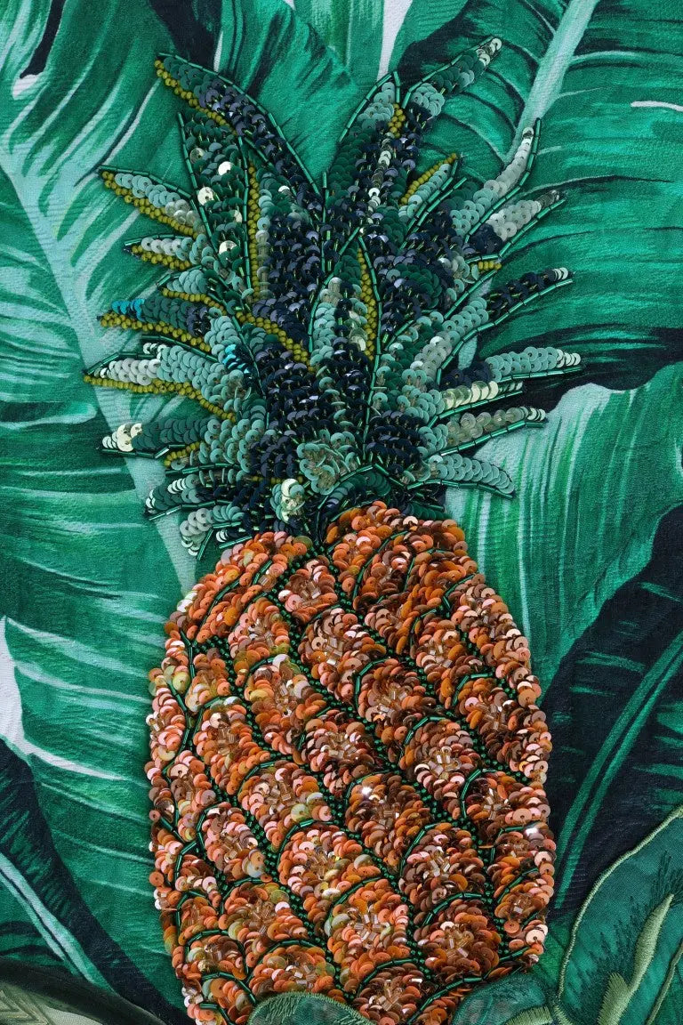 White crewneck sweater with green tropical leaves and a large sequin pineapple embellishment on front.