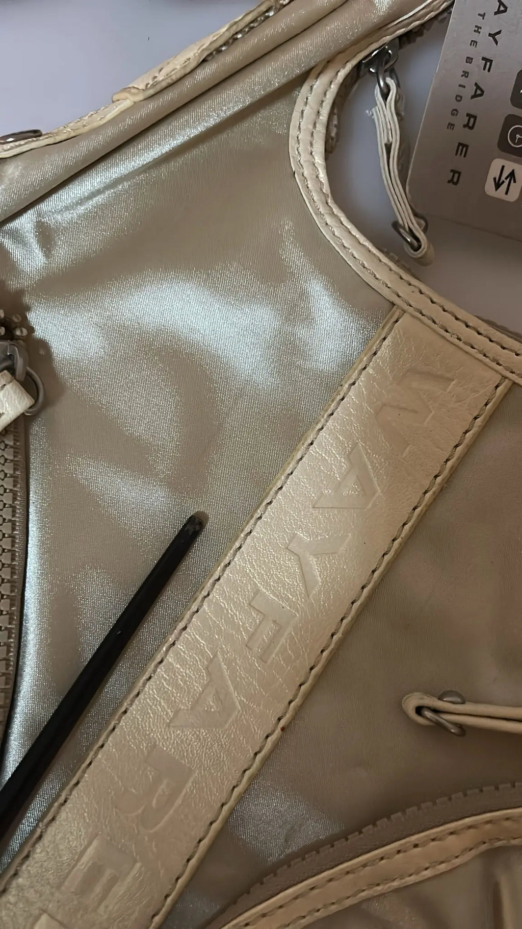 White fabric crossbody sling bag with beige trim and adjustable striped shoulder strap.